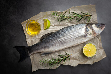 Raw seabass fish with rosemary and spices on dark background, top view
