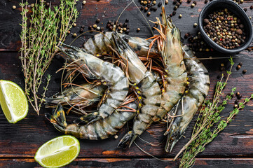 Black raw tiger prawns, shrimps with thyme and pepper. Black wooden background. Top view