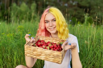Smiling teen girl with strawberries in basket, garden nature background