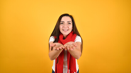 Portrait of beautiful woman blowing kiss against yellow background. Young brunette holds out her hands