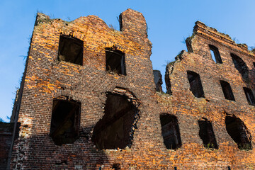 An old ruined building, without windows or doors, made of red bricks. The destroyed walls of the house