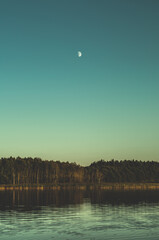 Wieczór nad jeziorem z księżycem nad lasem