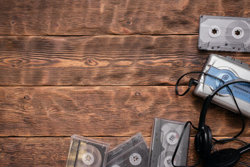 Portable retro stereo cassette player, old headphones and cassettes ont he brown wooden table...