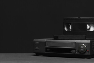 Video recorder and video tapes on the table on the black background.