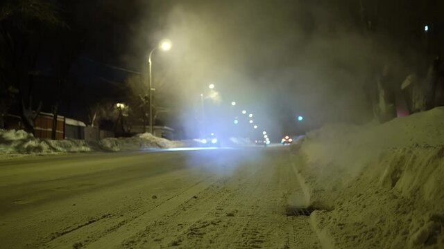 Russian winter road in the evening. Steam comes out of the sewer grate on the road