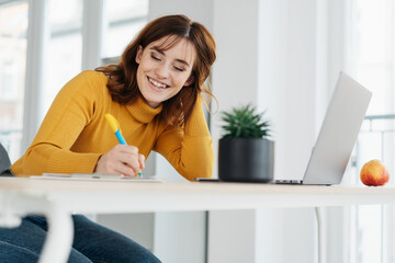 Happy young woman sitting writing at office table