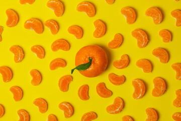 Tangerine with green leaf with peeled mandarin slices on yellow background. Color of the year 2021. Space for text. Top view