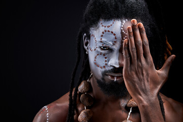 african maya man with national make-up closing half of face, portrait in studio on black...