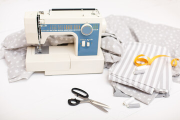 process of sewing of bed linen on sewing machine. Sewing kit. Grey fabric, scissors, threads, measuring tape and sewing machine on white wooden background