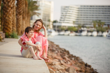 Son and mother walking on a beach near palm trees in casual outfit. Tropic vacation. Sea relax and rest. Spending a time on a beach. Smiling boy with his Dad together. Summer holiday sunny family day