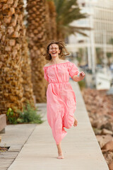 Young woman on a beach near palm trees in pink flying dress. Tropic vacation. Sea relax and rest. Spending a time on beach. Enjoying Happy time. Smiling female in lagoon. Summer holiday local tourism