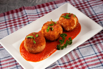 Delicious hot italian arancini - rice balls stuffed with cheese in tomato sauce, in a plate on an old wooden table
