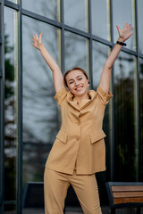 Business success - Happy young business woman celebrating work career achievements with both hands up against office building
