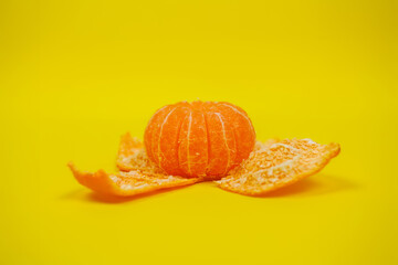 Peeled tangerine lies on a peel on a yellow background. Color of the year 2021. Space for text.