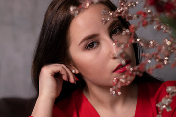 portrait of attractive brunette woman in red blouse near decorative sparkling red branches boquet. st valentines