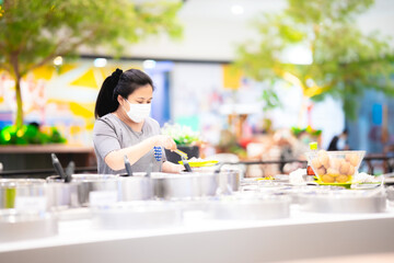 People were scooping up buffets at restaurants while the coronavirus outbreak. Woman wore mask to prevent saliva contamination into food pan while scooping. Take a social distance and a new lifestyle.