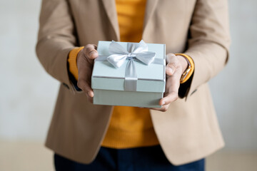 Hands of young elegant businessman passing you gift in blue box with bow