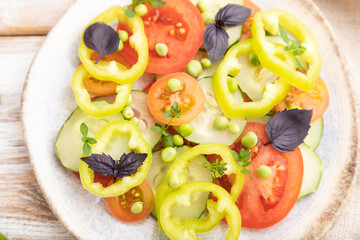 Vegetarian salad from green pea, tomatoes, pepper and basil on white wooden background. top view, close up, selective focus.