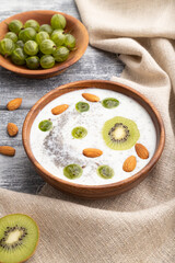Yogurt with kiwi, gooseberry, chia and almonds in wooden bowl on gray wooden background. Side view, close up.