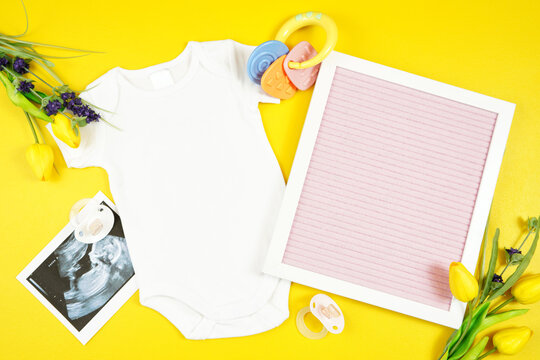 Springtime baby apparel flatlay on bright yellow table with colorful accessories. Mock up with negative copy space for your text or design here.