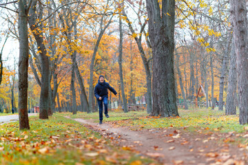 a boy running through the park and enjoys autumn, beautiful nature with yellow leaves