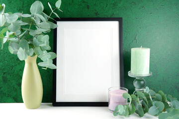 Picture Frame Mock up with eucalyptus leaves and candles, on a beautiful textured green background with negative copy space for your text or design here. Modern, stylish design.