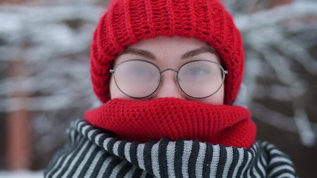 Portrait of a young woman in misted glasses outdoors on a frosty snowy day, camera zoom out