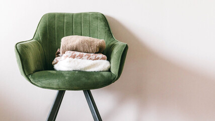 Stack of clothes on a green chair in a light room. Home space organization, spring cleaning and...