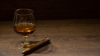 BOURBON GLASS WITH CIGAR ON RUSTIC WOOD TABLE AND LITTLE LIGHTING, WITH SPACE FOR TEXT