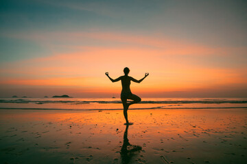 Fototapeta na wymiar An woman practicing yoga on the ocean side, the silhouette of awesome sunset.