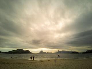 Beach before the storm. Sky with many tropical rain clouds and few people in the distance. Mountains of Rio de Janeiro city on the horizon.