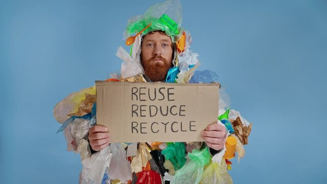 Man wearing trash costume, looking at the camera and holding cardboard plate with inscription reduse reuse recycle.