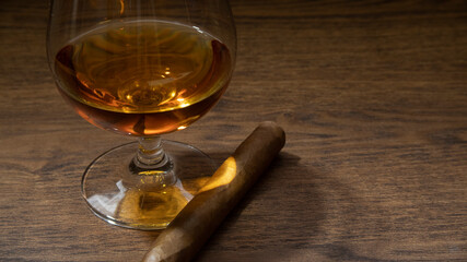BOURBON GLASS WITH CIGAR ON RUSTIC WOOD TABLE AND LITTLE LIGHTING, WITH SPACE FOR TEXT