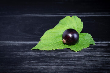 Black currant and green leaves on a dark wooden background. Background with currant berries and green leaves. Currant macro.
