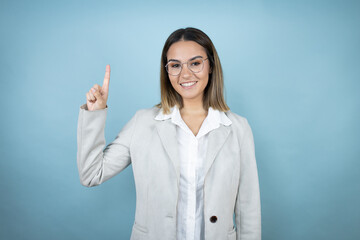 Young business woman over isolated blue background showing and pointing up with fingers number one while smiling confident and happy