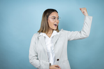 Young business woman over isolated blue background showing arms muscles smiling proud