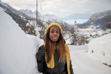 An African girl dressed heavily to withstand the cold, poses near a snow wall in the mountains.