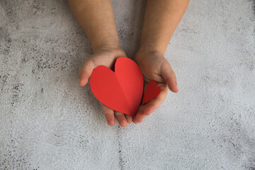 Two baby hands holding red paper hearts.
