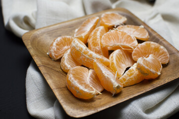 lateral view of mandarin segments in a wood bowl on white towel on black background.