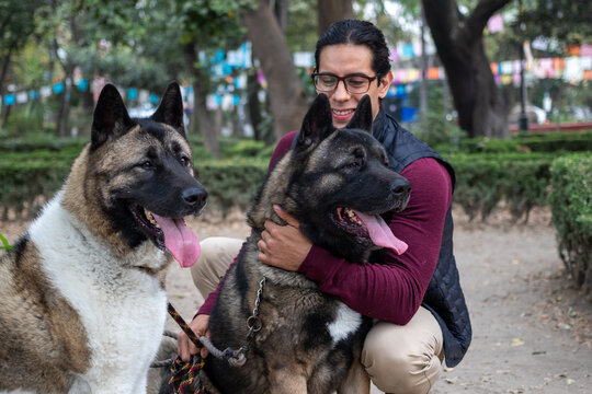Young hispanic man petting and holding his american akita dog in the park