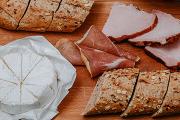 Baguette with sesame seeds and seeds, dark bread with camembert and meat on a board. Meat and cheese snack, breakfast. Nice photo of food. Snack delivery.