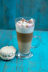 cappuccino in a transparent glass with marshmallows and cocoa powder on a blue wooden background