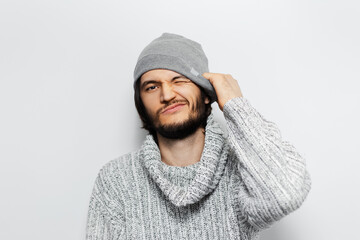 Close-up of young cheerful guy wearing grey hair and sweater on white background.