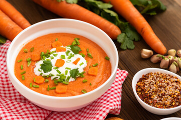 Delicious traditional carrot soup with herbs and sour cream on a wooden table.