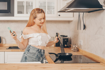 A girl in headphones with a phone stands in the kitchen and prepares food behind an induction stove. A woman searches for recipes on the Internet, watches a cooking show, listens to a podcast.