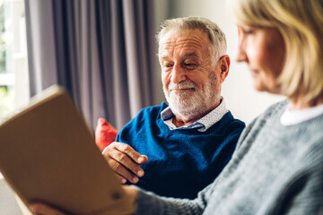 Senior couple family relax having good time reading the book together.Happy elderly husband and wife reading news and magazine while sitting on sofa at home.Retirement concept