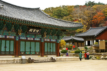 Obraz premium In Jogyesan Provincial Park, South Korea, visitors explore Seonamsa's weathered-wood temple buildings amid brilliant fall foliage.