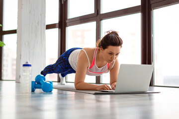 Fototapeta na wymiar Middle-aged woman exercising at home online in front of a laptop monitor. In plank position.