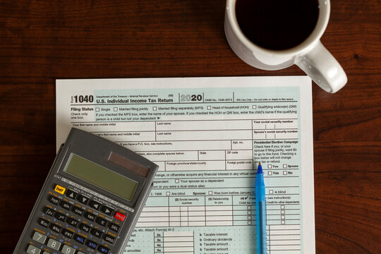 A simple versatile US federal income tax return concept image with an empty 1040 form on wooden table together with pen, marker, calculator, and a coffee mug. Do it yourself (DIY) idea..