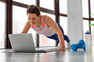 Fototapeta na wymiar Photo of a middle-aged woman doing push-ups at home in front of a laptop monitor.